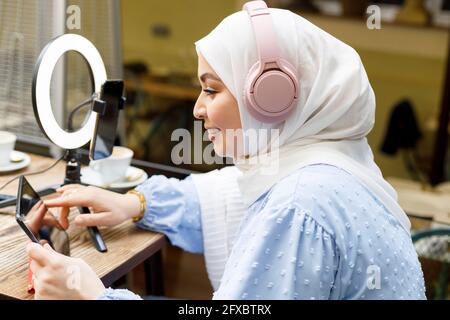 Female influencer wearing headphones using digital tablet while vlogging at cafe Stock Photo