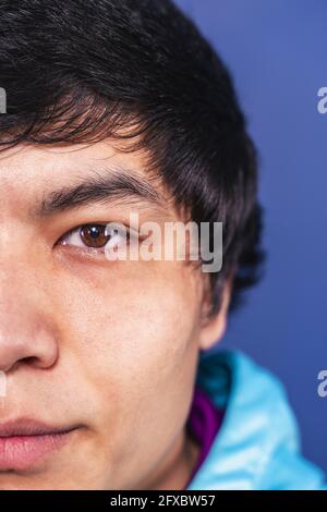 Young man with black hair in front of blue background Stock Photo