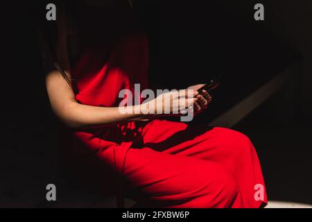 Unrecognizable businesswoman in shadow with a red dress holding her cell phone. Business concept. Stock Photo