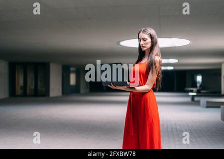 Young business woman in red dress and typing on her laptop standing up. Stock Photo
