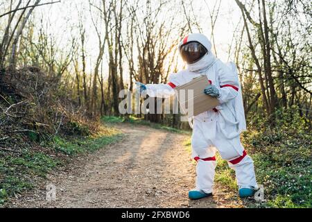 Female explorer in space suit standing with cardboard on dirt road Stock Photo