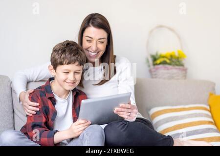 Smiling boy and mother using digital tablet on sofa at home Stock Photo