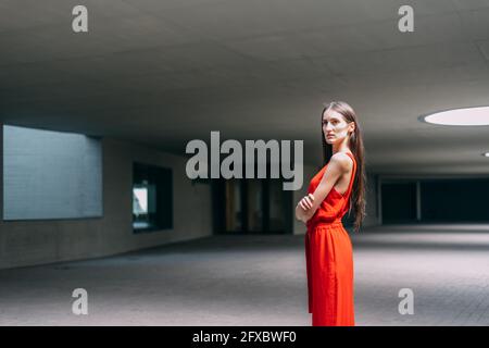 Businesswoman in red dress, arms crossed looking at camera indoors Stock Photo
