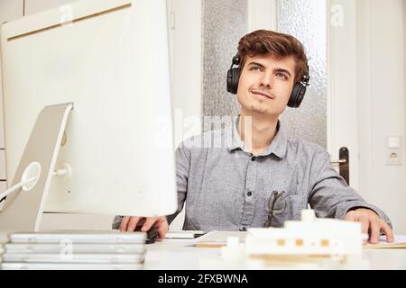 Male architect looking away while listening music through headphones at office Stock Photo
