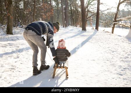 Father teaching sledding to son on snow during sunny day Stock Photo