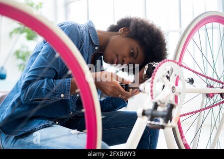 Young woman in casuals repairing bicycle at home Stock Photo