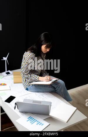 Female entrepreneur writing while sitting on desk at office Stock Photo