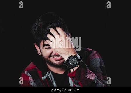 Smiling man with hand in hair over black background Stock Photo