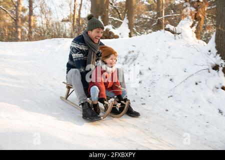 Playful father and son sledding on snow during winter Stock Photo