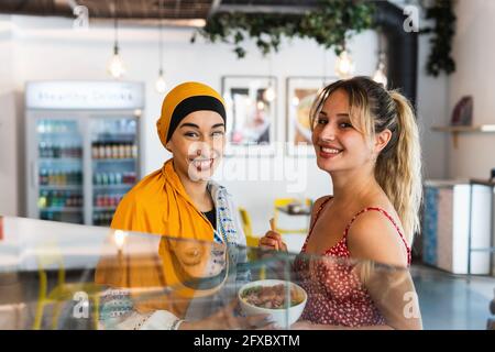 Smiling female friends holding poke bowl while standing in restaurant Stock Photo
