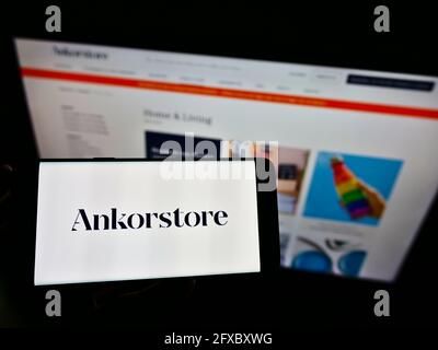 Person holding cellphone with logo of French online B2B wholesale company Ankorstore SAS on screen in front of web page. Focus on phone display. Stock Photo