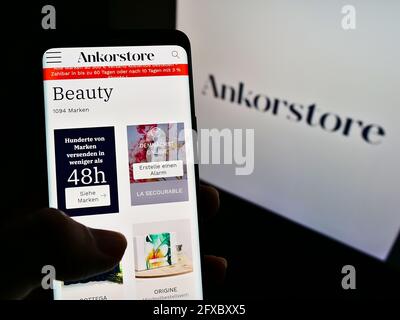 Person holding mobile phone with webpage of French B2B marketplace company Ankorstore on screen in front of logo. Focus on center of phone display. Stock Photo