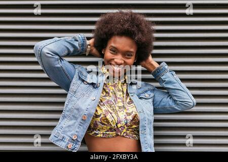 Happy woman with hands behind head in front of corrugated wall Stock Photo