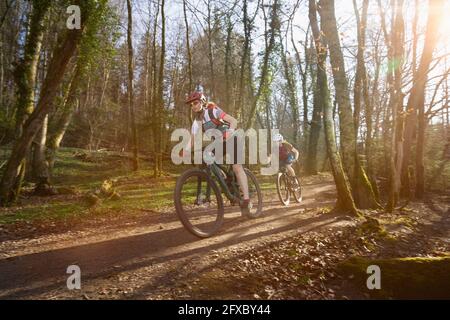 Female cyclists riding cycles on dirt road in forest Stock Photo