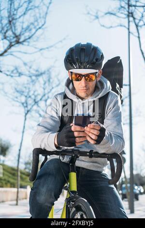 Mature delivery man leaning on bicycle while using smart phone Stock Photo