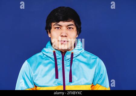 Young man wearing hooded shirt in front of blue background Stock Photo
