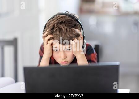 Tired boy attending remote classes through laptop at home Stock Photo