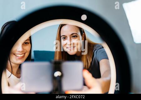 Smiling female influencers vlogging using mobile phone at home Stock Photo