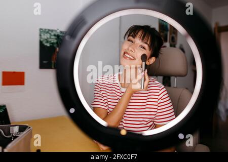 Beautiful female influencer applying blusher at studio Stock Photo