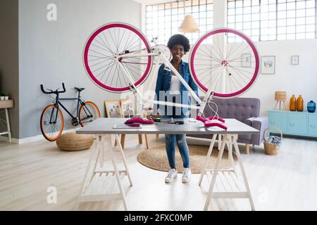 Smiling young woman with bicycle on table at home Stock Photo