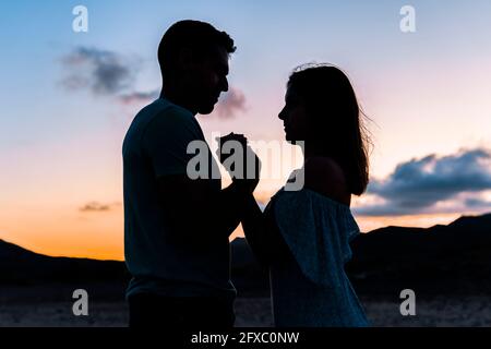 Couple holding hands while standing outdoors during sunset Stock Photo