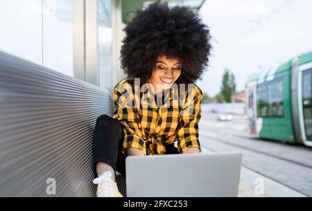 Smiling woman using laptop at railroad station Stock Photo
