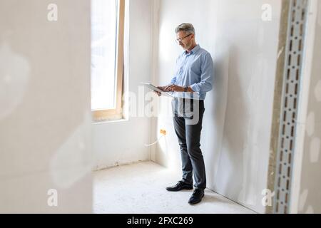 Male entrepreneur using digital tablet while standing by wall at construction site Stock Photo