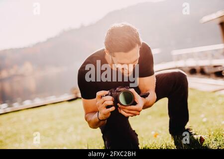 Young man crouching while using camera on lawn Stock Photo