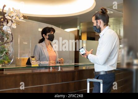 Male customer showing QR code to female receptionist in hotel during pandemic Stock Photo