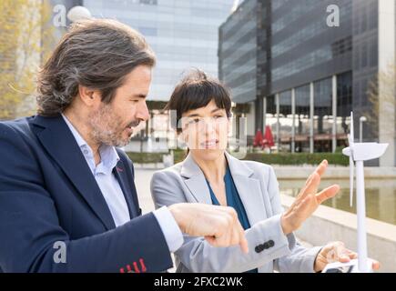 Male and female engineers discussing over wind turbine model in office park Stock Photo