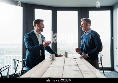 Smiling male professionals with coffee cup discussing at table at work place Stock Photo