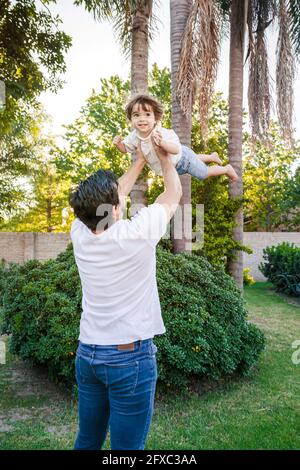 Mid adult man picking up baby boy while playing at back yard Stock Photo