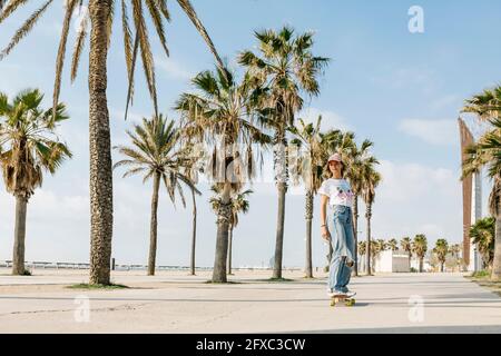 Mid adult woman skating by palm tree on footpath Stock Photo