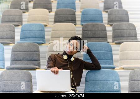 Curly haired woman using laptop at auditorium Stock Photo