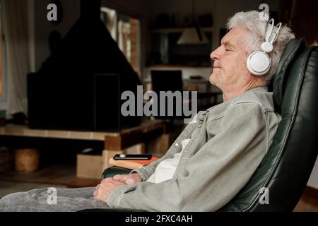 Senior man wearing headphones resting at home Stock Photo