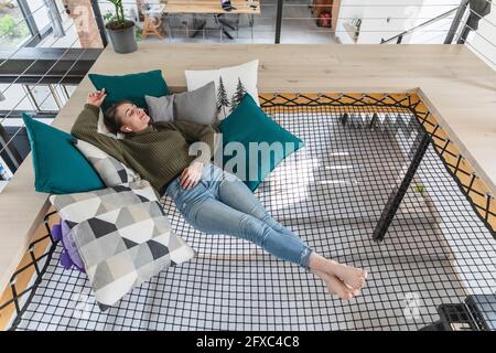 Relaxed young woman lying on hammock in modern home Stock Photo