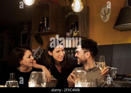 Female friends talking with smiling mature man while having drink at home Stock Photo