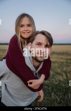 Father giving piggyback ride to daughter in field Stock Photo