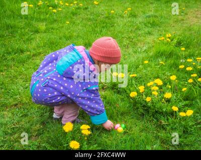 Girl wearing knit hat collecting Easter eggs at park Stock Photo