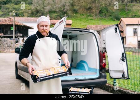 Male manager holding cheese tray by car on road Stock Photo