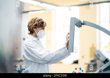 Female scientist with protective face mask using machine in laboratory Stock Photo