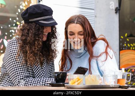 Smiling young women using mobile phone at sidewalk cafe Stock Photo