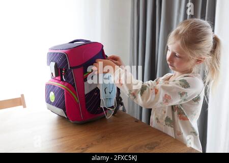 Face masks hanging on backpack at table Stock Photo