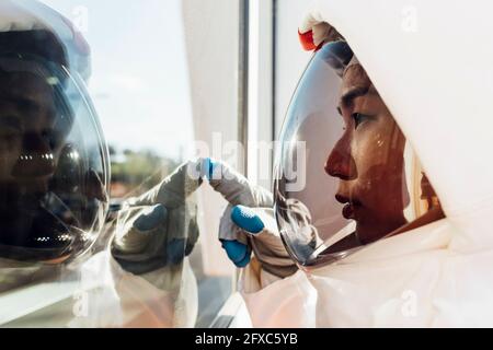 Young female astronaut in space helmet touching glass window Stock Photo