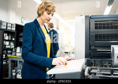 Female engineer using printing machine while working with colleague in industry Stock Photo
