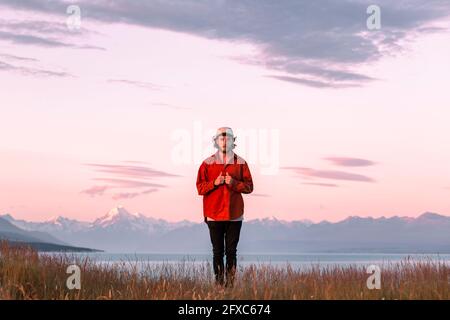 New Zealand, Canterbury, Front view of young man standing over Lake Pukaki at sunset Stock Photo