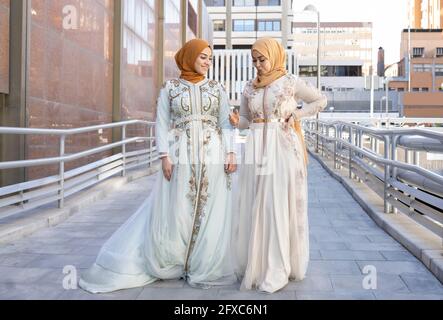 Young woman in fashionable dress talking with friend on bridge Stock Photo