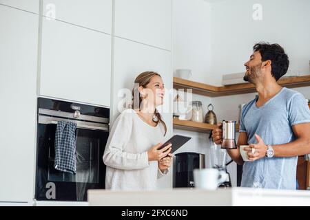 Cheerful young couple looking at each other while standing in domestic kitchen Stock Photo