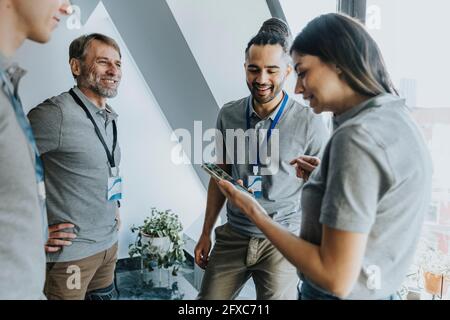 Smiling female professional discussing over mobile phone with male colleagues during conference Stock Photo