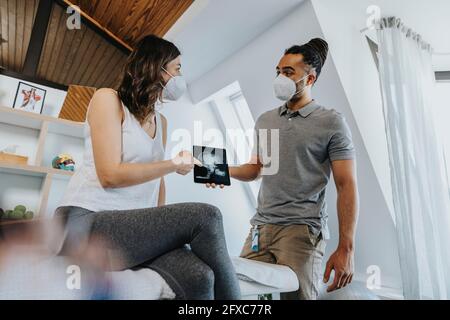 Female patient discussing over digital x-ray image with male physical therapist in practice during COVID-19 Stock Photo